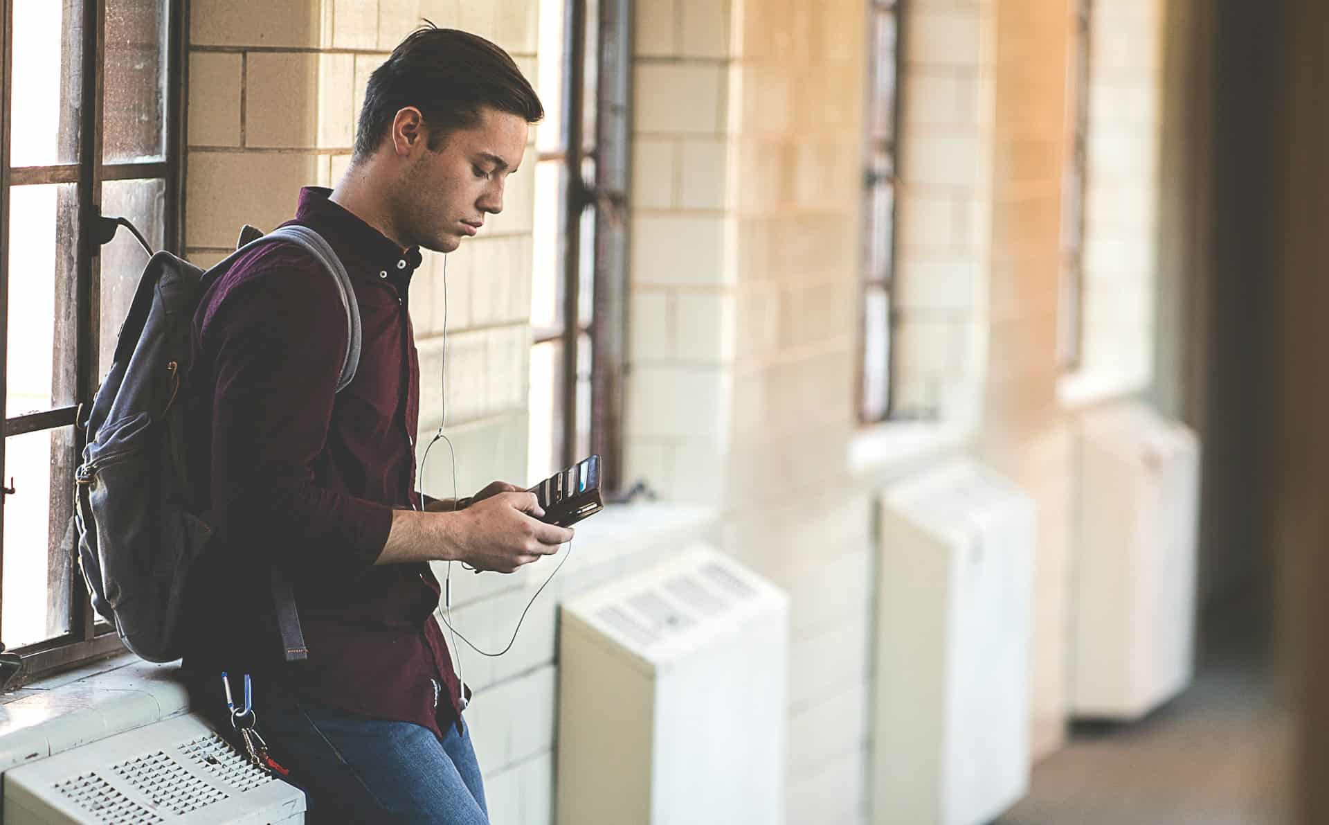 A student wearing a backpack uses his mobile phone