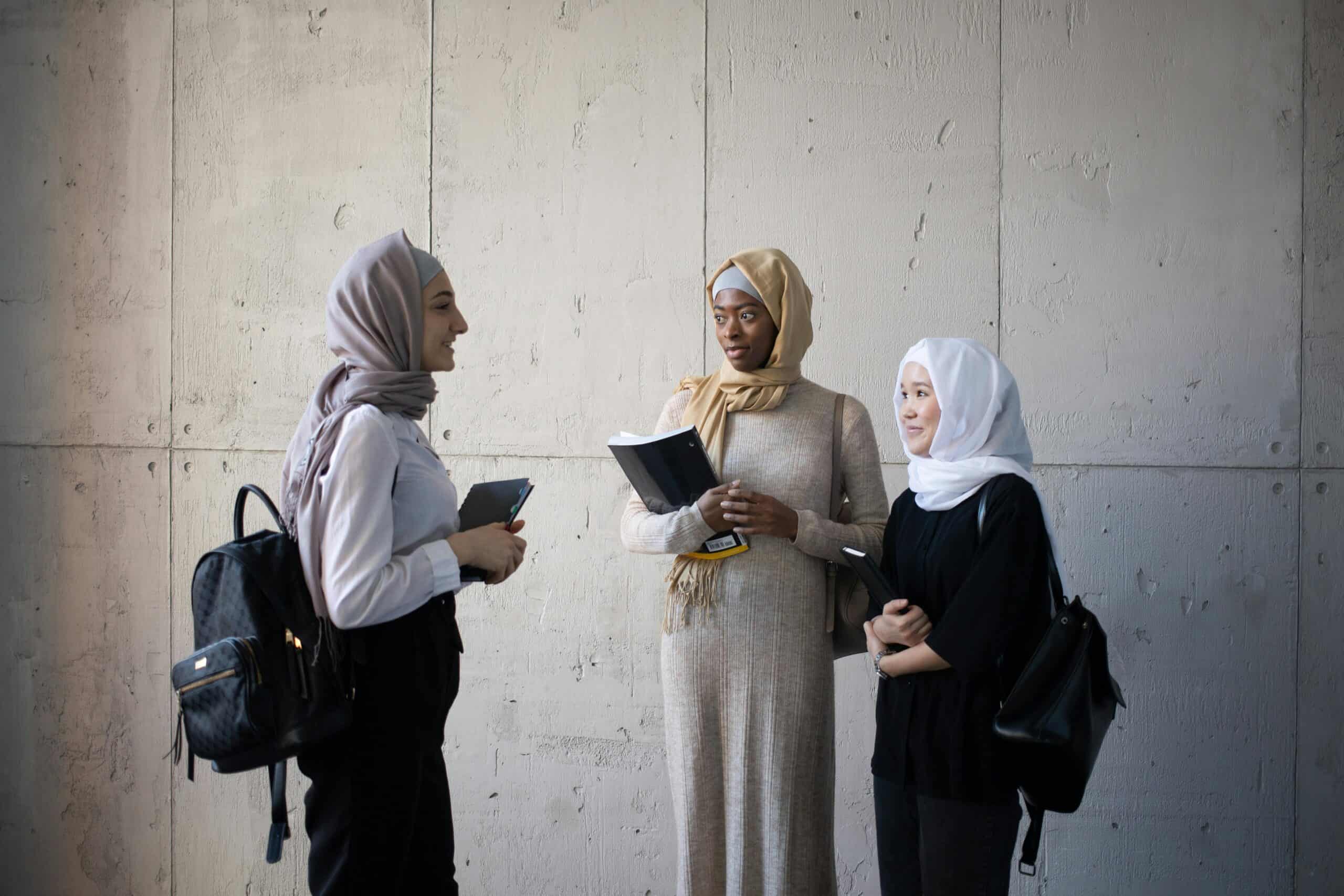 Three students stand in a hall chatting